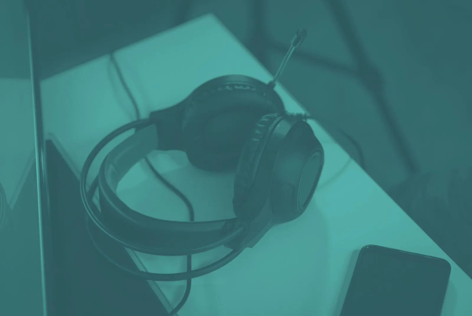 A headset with a microphone resting on a desk next to a phone