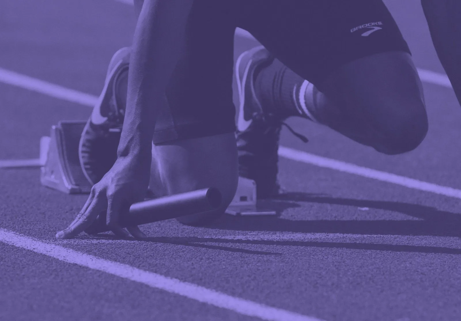 A sprinter in the starting blocks with a relay baton, ready to go